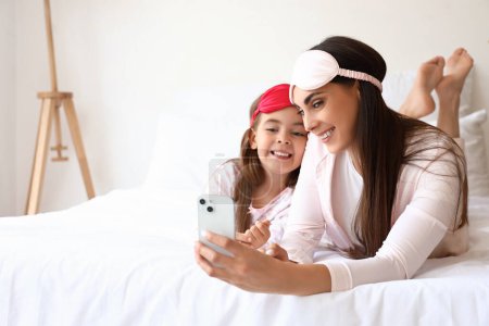 Téléchargez les photos : Mère heureuse et sa petite fille avec des masques de sommeil prenant selfie dans la chambre - en image libre de droit