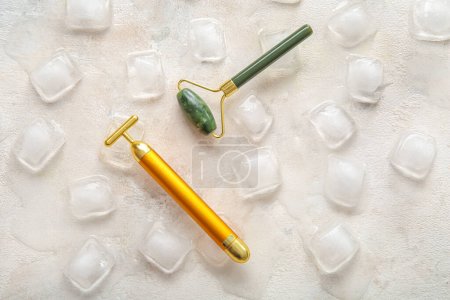 Foto de Diferentes rodillos de masaje facial con cubitos de hielo sobre fondo claro - Imagen libre de derechos