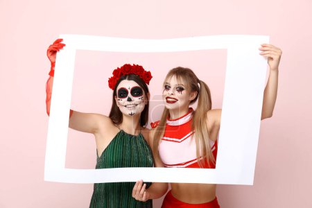 Foto de Amigas vestidas para Halloween con marco sobre fondo rosa - Imagen libre de derechos