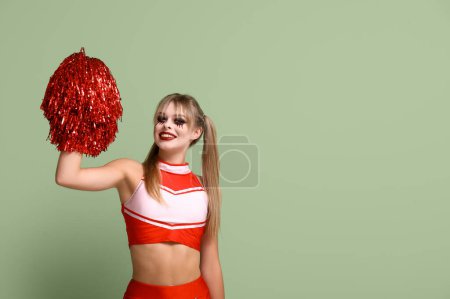 Young woman dressed for Halloween as cheerleader on green background