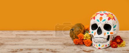 Calavera humana pintada para el Día de los Muertos de México (El Dia de Muertos), calabaza y flores sobre mesa sobre fondo naranja con espacio para texto