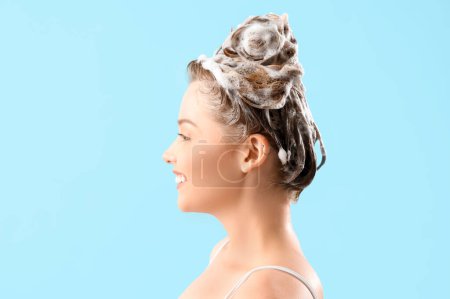 Young woman with shampoo on blue background, closeup