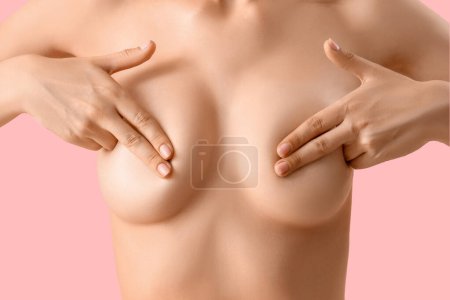 Mujer joven desnuda cubriendo su pecho sobre fondo rosa, primer plano