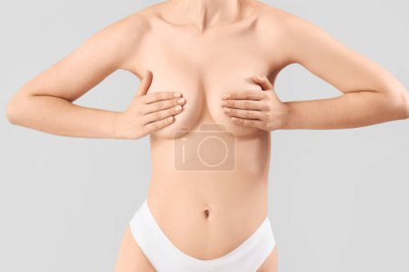 Téléchargez les photos : Jeune femme couvrant sa poitrine sur fond gris - en image libre de droit