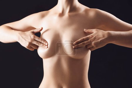 Téléchargez les photos : Jeune femme nue couvrant sa poitrine sur fond noir - en image libre de droit
