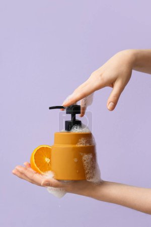 Mains avec savon liquide et orange sur fond lilas