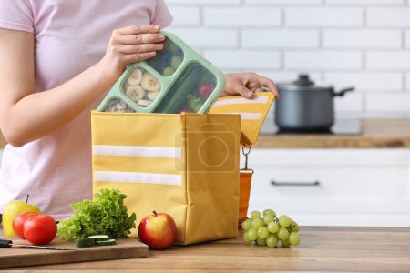Téléchargez les photos : Femme emballant le repas frais dans le sac de boîte à lunch dans la cuisine - en image libre de droit