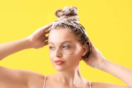 Mujer joven lavando el cabello sobre fondo amarillo, primer plano