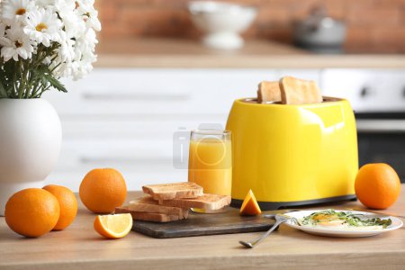 Téléchargez les photos : Grille-pain moderne, verre de jus, oranges et œufs frits sur la table dans la cuisine - en image libre de droit