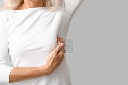 Foto de Mujer madura revisando su pecho sobre fondo gris, primer plano. Concepto de concienciación - Imagen libre de derechos