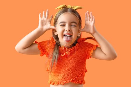 Téléchargez les photos : Petite fille mignonne montrant la langue sur fond orange - en image libre de droit