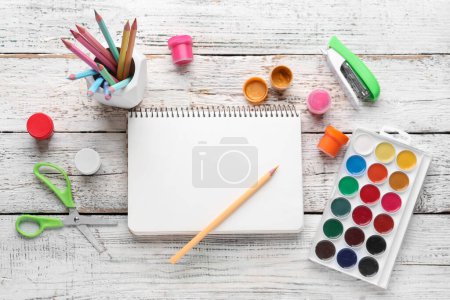 Foto de Composición con cuaderno en blanco, lápices de color y pinturas sobre fondo de madera blanco - Imagen libre de derechos