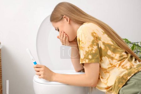 Téléchargez les photos : Jeune femme enceinte avec test souffrant de toxicose près de la cuvette des toilettes dans les toilettes - en image libre de droit