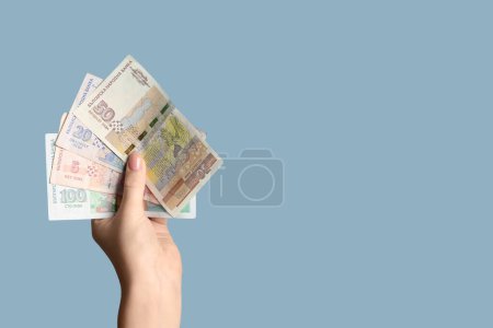 Female hand holding Bulgarian lev banknotes on blue background