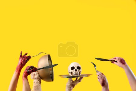 Téléchargez les photos : Zombie mains tenant cloche avec crâne et couverts sur fond jaune. Fête d'Halloween - en image libre de droit