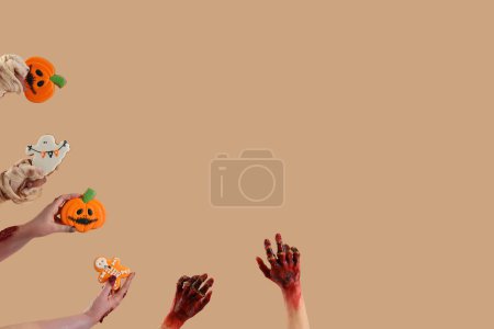 Téléchargez les photos : Zombie et momie mains tenant des biscuits d'Halloween sur fond beige - en image libre de droit
