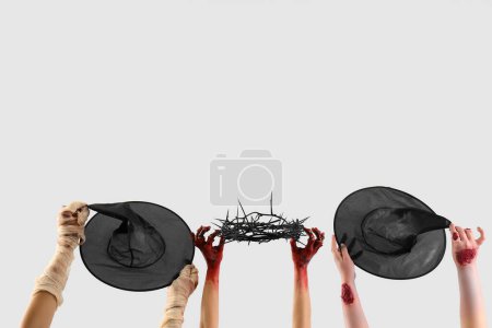 Photo for Zombie hands holding witch hats and crown of thorns on white background. Halloween celebration - Royalty Free Image
