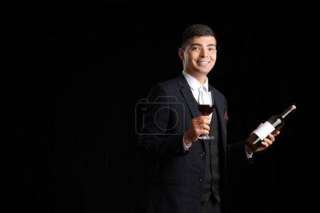 Photo for Young sommelier with glass and bottle of wine on black background - Royalty Free Image