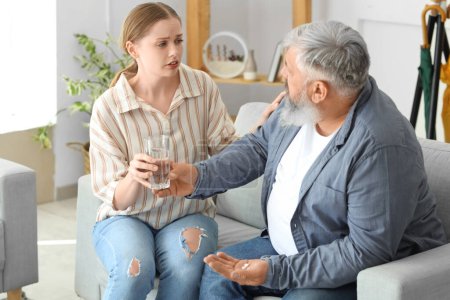 Photo for Young woman giving medicine to her father who is having heart attack at home - Royalty Free Image