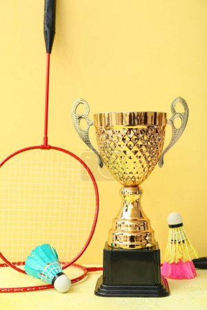 Photo for Gold cup with badminton rackets and shuttlecocks on yellow background - Royalty Free Image