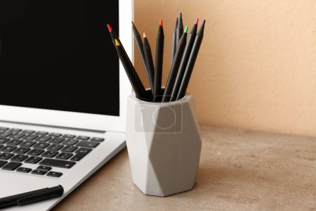 Foto de Portátil moderno y soporte con diferentes lápices en el escritorio, primer plano - Imagen libre de derechos