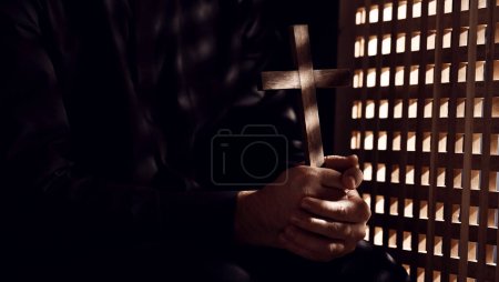 Photo for Young priest with cross in confession booth - Royalty Free Image