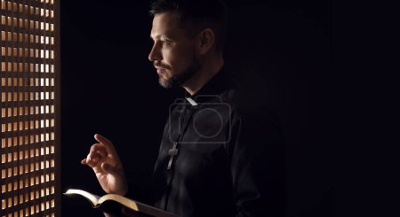 Photo for Male priest with Bible in confession booth - Royalty Free Image
