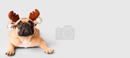 Foto de Lindo perro con cuernos de reno y bolas de Navidad sobre fondo claro con espacio para texto - Imagen libre de derechos