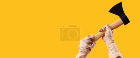 Téléchargez les photos : Mains momie avec hache sur fond jaune avec espace pour le texte. Fête d'Halloween - en image libre de droit