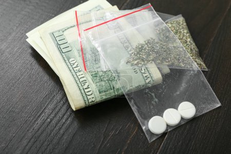 Foto de Bolsas de plástico con drogas y dinero sobre fondo de madera oscura - Imagen libre de derechos