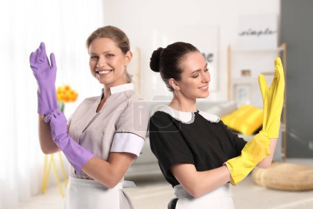 Photo for Portrait of beautiful chambermaids putting on rubber gloves before cleaning living-room - Royalty Free Image