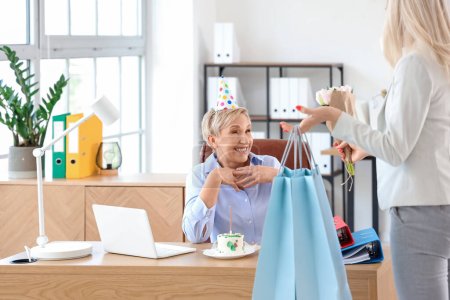 Mature woman receiving birthday gifts from her colleague in office