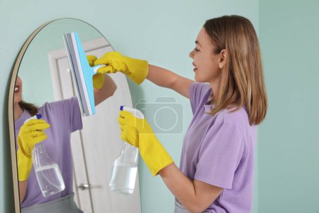 Photo for Young woman cleaning mirror with squeegee in bathroom - Royalty Free Image