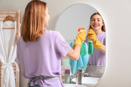 Photo for Young woman cleaning mirror in bathroom - Royalty Free Image