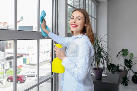 Photo for Young woman cleaning window in office - Royalty Free Image