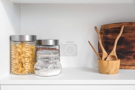 Téléchargez les photos : Etagère blanche avec planche à découper, cuillères et bocaux en bois - en image libre de droit