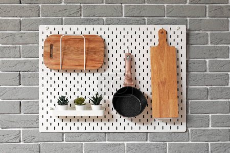 Téléchargez les photos : Pegboard avec planches à découper, poêle à frire et plantes d'intérieur suspendues au mur de briques grises - en image libre de droit