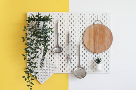 Téléchargez les photos : Pegboard blanc avec planche à découper, plantes d'intérieur et ustensiles suspendus au mur de couleur - en image libre de droit