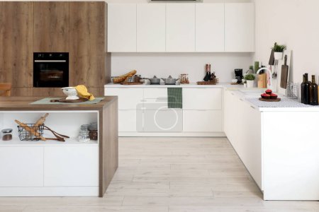 Téléchargez les photos : Intérieur de la cuisine moderne avec comptoirs blancs, placards et table îlot en bois - en image libre de droit