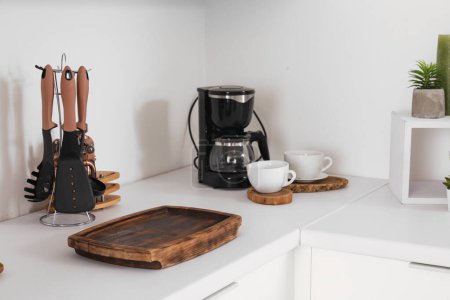 Téléchargez les photos : Comptoir de cuisine blanc avec planche à découper, machine à café, tasses et ustensiles - en image libre de droit