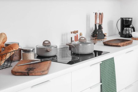 Téléchargez les photos : Comptoirs de cuisine blancs avec planches à découper, cuisinière électrique, casseroles et ustensiles de cuisine - en image libre de droit