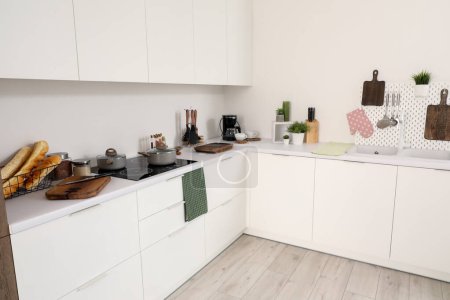 Téléchargez les photos : Intérieur de la cuisine légère avec planches à découper, pegboard, évier et cuisinière électrique sur comptoirs blancs - en image libre de droit