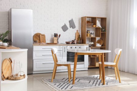 Téléchargez les photos : Intérieur de la cuisine lumineuse avec comptoirs blancs, réfrigérateur et table à manger - en image libre de droit