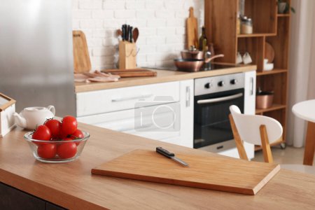 Téléchargez les photos : Planche à découper en bois avec couteau et tomates fraîches sur la table dans la cuisine moderne - en image libre de droit
