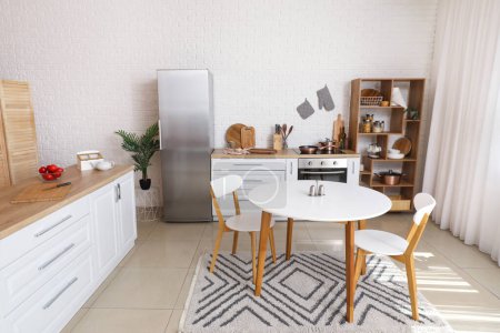 Téléchargez les photos : Intérieur de la cuisine lumineuse avec comptoirs blancs, réfrigérateur et table à manger - en image libre de droit