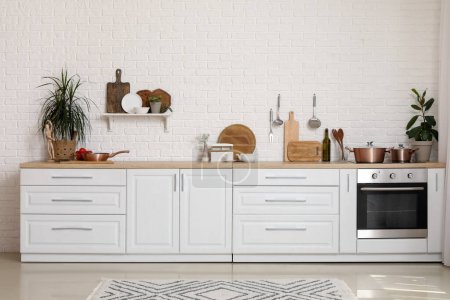 Téléchargez les photos : Comptoirs blancs avec planches à découper, ustensiles, plantes d'intérieur et cuisinière électrique dans la cuisine moderne - en image libre de droit