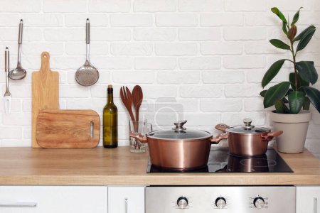 Téléchargez les photos : Comptoirs en bois avec planches à découper, ustensiles, plantes d'intérieur et cuisinière électrique dans la cuisine moderne - en image libre de droit