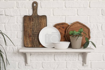 Téléchargez les photos : Étagère de cuisine avec planches à découper, assiette, bol et plante d'intérieur suspendue au mur de briques blanches - en image libre de droit