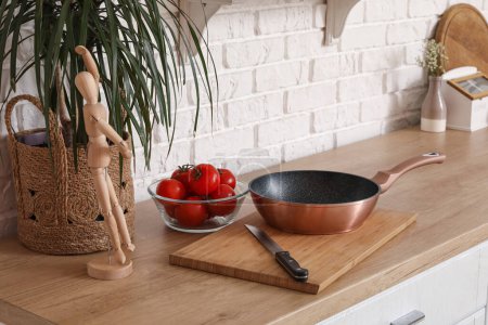 Téléchargez les photos : Comptoir en bois avec planche à découper, couteau, tomates fraîches et poêle dans la cuisine moderne - en image libre de droit