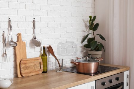Wooden counters with cutting boards, utensils, houseplant and electric stove in modern kitchen